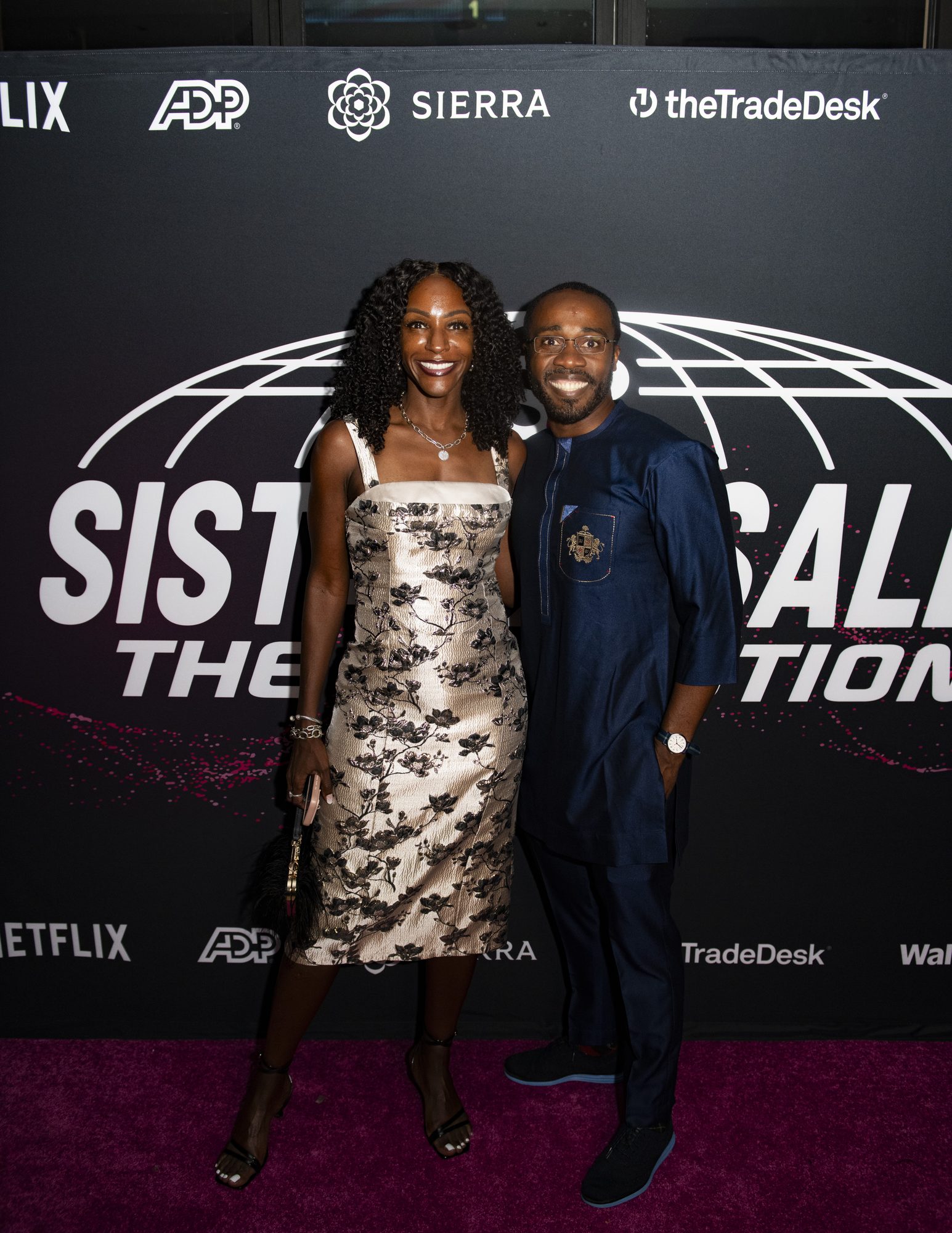 Two guests posing on the pink carpet at the step-and-repeat with partner logos