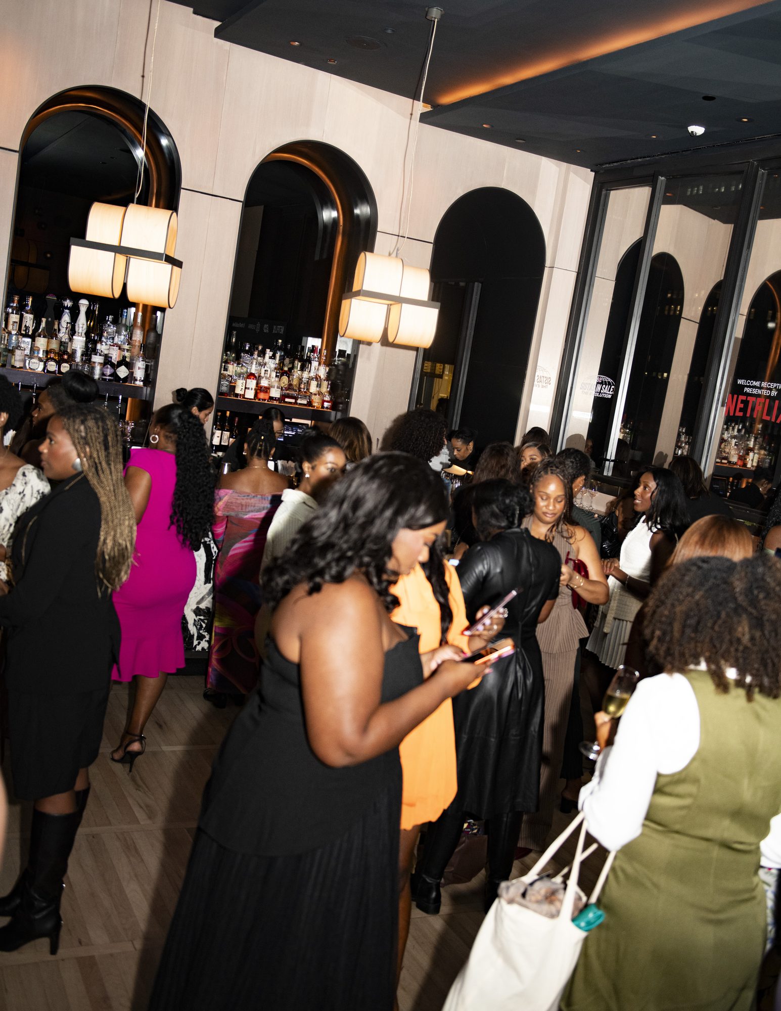 Full room of guests gathered by the bar under arched windows