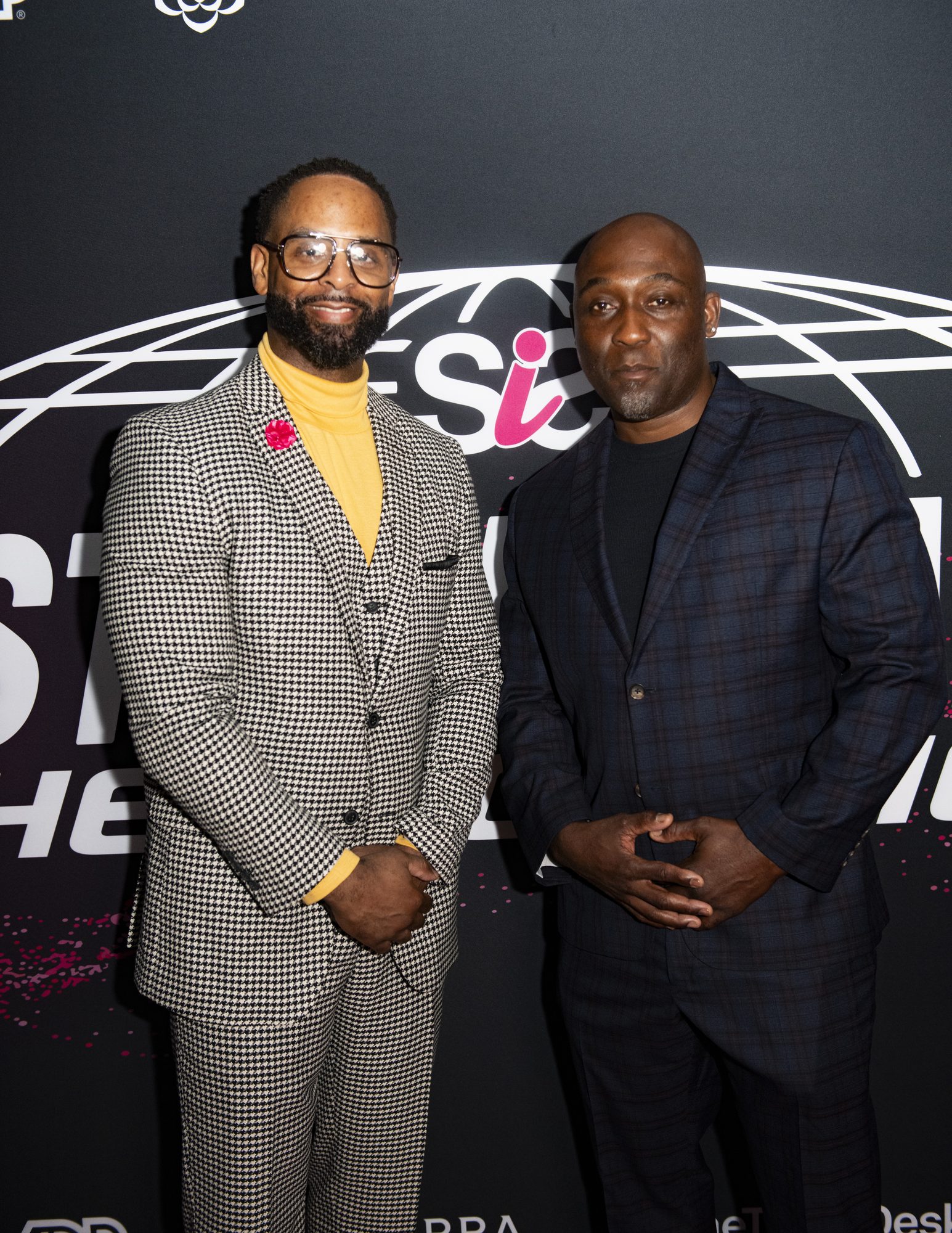 Two guests in suits posing at the Sistas in Sales: The Evolution step-and-repeat