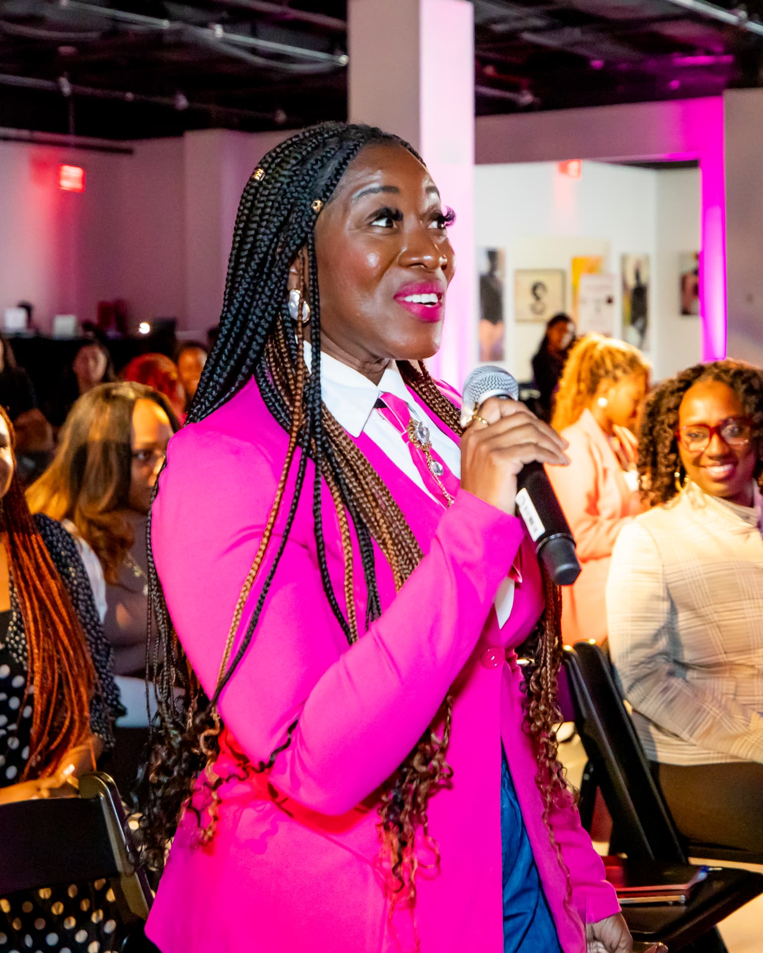 SIS attendee in a hot pink power suit with a white collared shirt and pink tie, speaking into a microphone